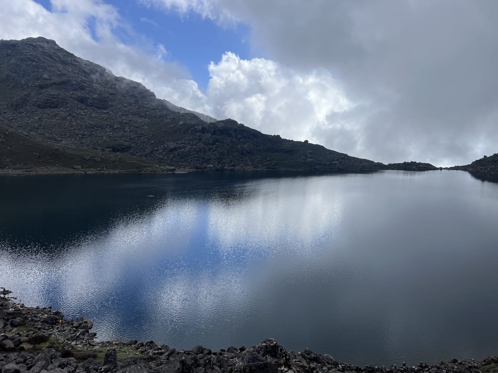 A still mountain lake reflecting a grey sky and rocky hills